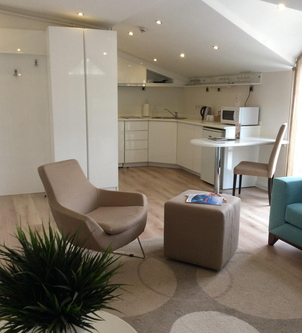 Apartment lounge with armchairs and a fully fitted kitchenette behind